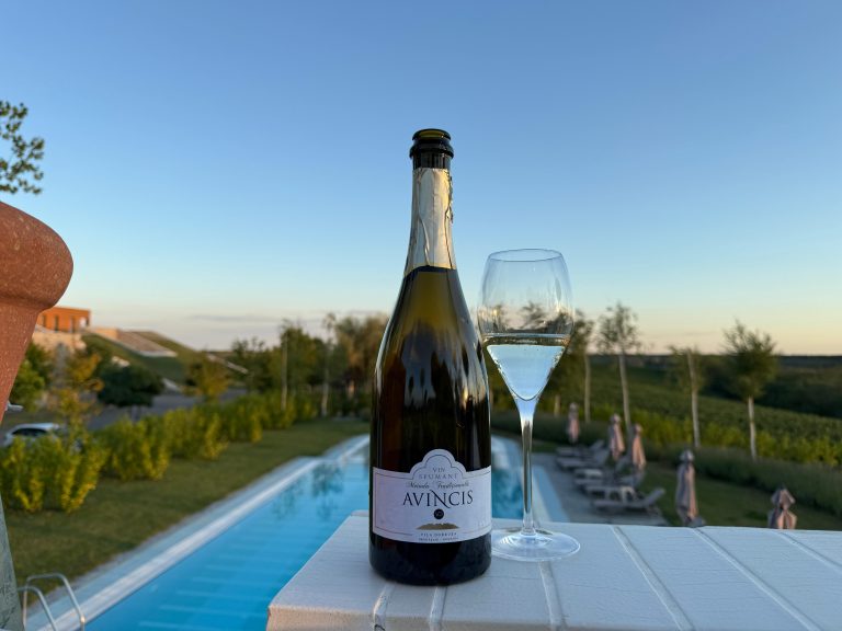 Sticlă de vin spumant Avincis și pahar pe terasa Domeniului Vila Dobrușa din Drăgășani