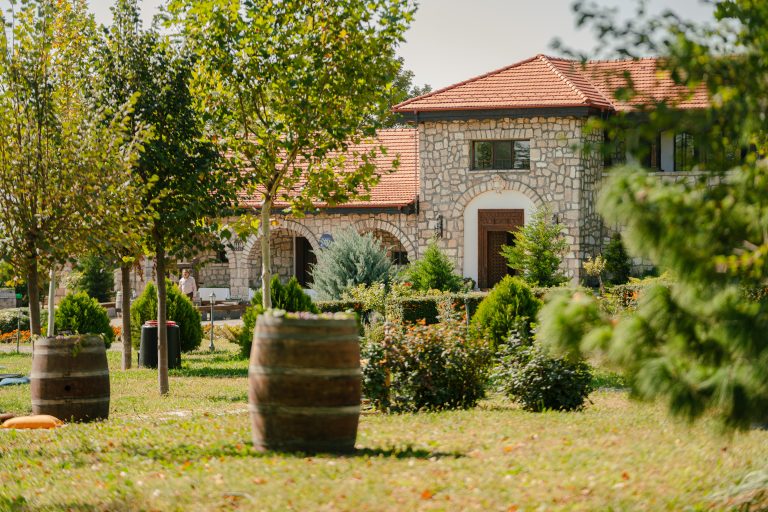 Conac din piatră tradițională &icirc;n Dealu Mare, &icirc;nconjurat de grădini verzi și butoaie de lemn