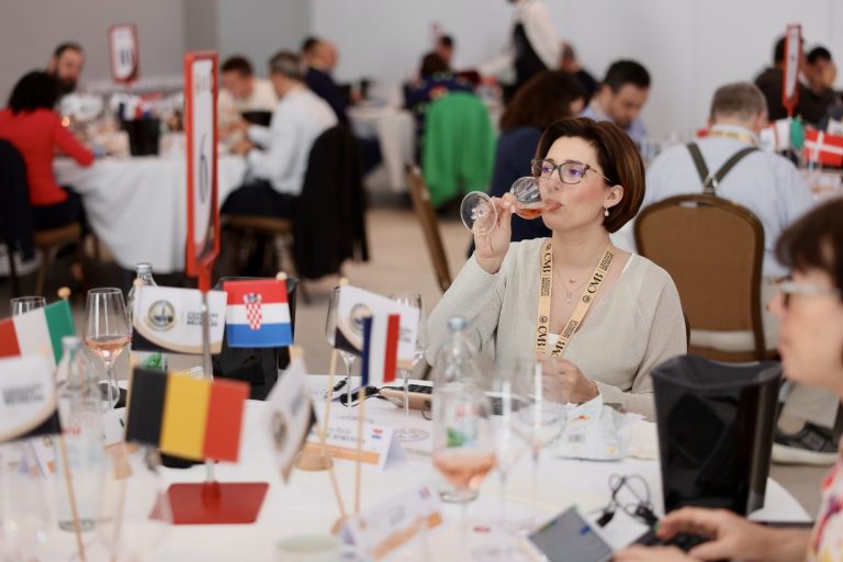 Degustătoare de vin ros&eacute; &icirc;n cadrul Concours Mondial de Bruxelles, la o masă cu stegulețe internaționale.