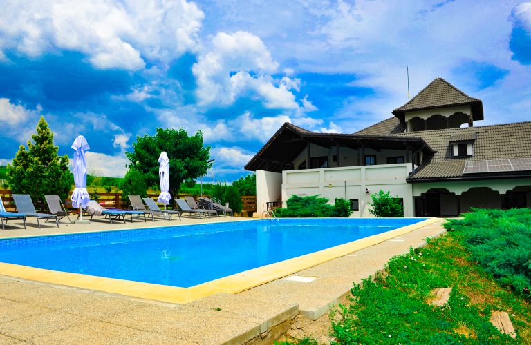 Piscină modernă la o cramă din Dealu Mare, &icirc;nconjurată de verdeață și clădire tradițională