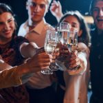 Grup de tineri ciocnind pahare de vin spumant la o petrecere de seară