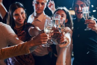 Grup de tineri ciocnind pahare de vin spumant la o petrecere de seară