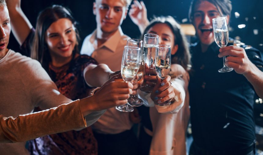 Grup de tineri ciocnind pahare de vin spumant la o petrecere de seară