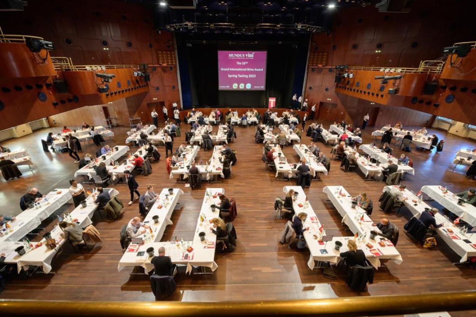 Sala de degustare a concursului internațional de vinuri Mundus Vini 2023, cu zeci de jurați evaluând probe de vin.