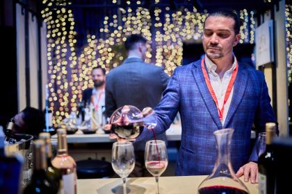 Vinuri românești de descoperit: Ce noutăți am gustat la RO-Wine 2025 Meta descriere Descoperă cele mai interesante vinuri românești prezentate la festivalul RO-Wine 2025 – ediția de toamnă. Jidvei, SERVE, Vintruvian, Gramofon și multe alte crame au adus vinuri de colecție și experiențe memorabile. RO-Wine 2025: un festival al descoperirilor de toamnă Tradiția festivalurilor de vin spune că primăvara îți prezinți vinurile albe, pentru vara care se apropie, iar toamna – vinurile roșii din recolta anului trecut. Doar că producătorii noștri au înțeles repede că festivalurile atrag un alt public, de la profesioniștii din horeca, interesați de vinuri speciale, la iubitorii de vin care își caută vinuri pentru colecții, pentru seri speciale alături de prieteni sau de savurat pe îndelete. Așa că tradiția vinurilor proaspete a început să se estompeze, iar oferta prezentată să aducă tot mai des, alături de noutăți, vinuri mai vechi, unele chiar nelansate, care mai au nevoie de ceva timp „ca să se așeze”. Așa că, pe scurt, vă spunem mai jos la ce noutăți vă puteți aștepta în perioada următoare. Vinuri excelente, care le fac cinste producătorilor și care ne pot reprezenta oriunde în lume sau care deja au fost medaliate la concursuri importante. Jidvei – colecția Spirit și vinuri românești premiate internațional Spirit – trei vinuri speciale Jidvei a adus în premieră gama Spirit, o colecție de trei vinuri speciale – Chardonnay 2023 (baricat 6 luni), Fetească regală 2023 (baricată tot șase luni, dar în butoaie aflate la a doua întrebuințare) și un cupaj rose de Pinot noir, Syrah și Cabernet Sauvignon. Dacă Chardonnay-ul este oarecum previzibil, în notele clasice deja cunoscute – bun, gustos, rotund, cu accentele de lemn perfect integrate, Feteasca regală este o surpriză foarte plăcută și extrem de elegantă. Alegerea unor butoaie care transferă vinului mai puține arome s-a dovedit inspirată – vinul a câștigat note delicate dar, în același timp, și-a amplificat propriile resurse aromatice, prin ușoara microoxidare care are loc în timpul maturării în vase de stejar. Rezultatul nu este doar încântător, are și un potențial serios de învechire. Vinarsul XO – eleganță și rafinament Vizitatorii au mai avut ocazia să guste și ediția limitată a vinarsului Jidvei XO, pe care puțini au avut ocazia să-l descopere până acum și care nu a fost produs decât într-o ediție limitată de 5.000 de sticle. Produs exclusiv din Fetească regală, maturat mai mult de zece ani în butoaie de stejar, vinarsul are nuanțe intense de caramel, lemn nobil și mirodenii, cu nuanțe de tabac și scorțișoară. Dulce-picant și delicios. Owner’s Reserve Ana Fetească Regală + bule Mysterium Nou pe piață este și Owner's Reserve Ana Fetească regală, medaliat cu aur la Mundus vini, în această vară, încă de dinainte de lansare. Iar pentru amatorii de bule – recent lansatul spumant Mysterium 2021, un cupaj clasic de Pinot noir și Chardonnay, cu un strop de Fetească regală, pentru un accent local. Domeniul Bogdan – vinuri biodinamice și experiențe noi pentru iubitorii de vin Trufaș – Cabernet Sauvignon cu aromă subtilă de trufe negre Atracția standului la Domeniul Bogdan a fost, oarecum previzibil, Trufaș, un Cabernet Sauvignon aromatizat cu trufe negre, chiar dacă nu este chiar o noutate. Cu aromele de trufă păstrate discret, în fundal, vinul este dominat de fructe negre și ciocolată, cu accente picante și este, într-adevăr, un vin de top. Cuvée Experience roșu 2022 și Feteasca Neagră Pătrar 2020 Doar că, mai interesați de noutăți, ne-am oprit mai mult asupra Cuvée Experience roșu 2022, un cupaj de Fetească neagră și Merlot perfect echilibrat, suculent, plin de note de vișine și fructe negre, cu prune uscate pe final, o aciditate sănătoasă, care îi dă perspective bune de învechire pentru următorii ani. Remarcabilă, de asemenea, este și Feteasca neagră Pătrar din 2020, care abia intră în perioada de maturitate, deși poartă, încă din primul an, accente de fruct supracopt, dar bine ascuns de accentele de cacao, cireșe amare și prune de magiun. Domeniile Averești – Cabernetul de aur și Zghihara, vedetele Moldovei Un Cabernet de zonă răcoroasă Deși se spune că Moldova este mai degrabă potrivită pentru vinuri albe, Cabernetul sauvignon magnum Diamond Selection din 2019 este o minunăție de vin. Mătăsos, întunecat, cu note de pământ reavăn, afine, coacăze și mure, un pic de dulceață de cireșe amare, totul perfect integrat și cu o băubilitate rară. Nu e de mirare că a câștigat anul trecut aur la Concurs Mondial de Bruxelles, deși abia acum începe să-și dezvăluie potențialul. Zghihara 2024 – vin românesc versatil, plin de prospețime și echilibru Noutatea principală a fost, însă, Zghihara 2024 – tot magnum, și tot Diamond Selection – probabil unul dintre cele mai versatile vinuri din festival. Bun și de sete, și de acompaniat mâncăruri fine, și de seri lungi cu prietenii și pentru orice alte ocazii. Suficient de complex cât „să te țină de vorbă”, dar nu atât de intruziv cât să devină centrul atenției... Syrah de Vrancea de la Beciul Domnesc Cele mai vechi vinarsuri românești La Beciul Domnesc, atracția a fost, destul de clar împărțită între Jad și Miorița XO, două vinarsuri vechi, care stau oricând alături de orice distilat de vin din lume, dar și de gama Verité, cu un Blanc și un Rosé de excepție, cu un raport excelent calitate/preț. Cuveé 49, din nou, a confirmat că are o evoluție foarte bună. Syrah Grand Reserve – un debut promițător, cu potențial de colecție Surpriza, însă, a fost un Syrah Grand Reserve, primul exemplar din acest soi introdus în gama de top a producătorului. Bine echilibrat, plin de fruct, cu aciditatea specifică zonei bine integrată și un final elegant, Syrah promite să devină nu doar o prezență constantă în gamă, ci și un vin pentru colecționari și cunoscători. Deocamdată este încă tânăr, dar cu un potențial clar, numai bun de urmărit cum evoluează în următorii ani. Gramofon Wine: un Cabernet cald pentru zilele reci Nu s-a lansat (încă) distilatul Gramofon La Gramofon, din păcate, așteptata avanpremieră a primului distilat de vin s-a lăsat așteptată – o intervenție în ultima secundă, chiar când etichetele plecau spre tipografie, a dus la reconsiderarea brandului. Ceea ce, de fapt, nu înseamnă decât că lansarea va avea loc așa cum a fost anunțată, spre sfârșitul anului. Curioșii au avut, totuși, deja ocazia să guste vinarsul Gramofon în timpul celebrelor petreceri organizate la cramă. Cabernet 2022, premiera toamnei Alături de deja cunoscutele Sonorum și Cuveé roșu, Gramofon Wine a prezentat un singur vin în premieră, însă unul excepțional – Cabernet Sauvignon 2022, o demonstrație de eleganță, elocvență și măiestrie. Perfect echilibrat și rotunjit, jucăuș, într-un dans continuu între aromele de fruct, cele de condimente și notele de cacao, ciocolată și vanilie, este un vin care poate juca rolul de „vin de zi cu zi” pentru pofticioși, sau de vin pentru ocazii speciale, pentru consumatorii ocazionali. Vintruvian Estates – patru crame românești unite de calitate Cele mai vizitate standuri Despre grupul Vintruvian Estates, care reunește patru crame – Caii de la Letea Sarica Niculițel și Crama Histria în Dobrogea, Crama DeMatei în Dealu Mare și Oenoterra în Drăgășani – este greu de spus altceva decât că a avut în permanență cele mai aglomerate standuri. Au fost prezente vinuri de top, vinuri pentru toate gusturile, de la fresh la vinuri mature și complexe, de la vinuri accesibile la rarități de colecție – de la vinurile DeMatei notate de James Suckling cu 90-95 de puncte la noile Scoarțe de la Oenoterra, o Crâmpoșie și un Negru de Drăgășani potrivite pentru orice ocazie. Au revenit „Trilogiile” Pentru că ne concentrăm, totuși, pe noutăți, trebuie neapărat să încercați „Trilogiile” (alb, rosé și roșu) revenite între gamele Caii de la Letea, după o scurtă absență. Cu o mențiune specială pentru Trilogia în roșu, unde au fost folosite vinuri din regiuni diferite – Negru de Drăgășani, Băbească neagră și Fetească neagră. Un vin excelent, plin de nuanțe, de savurat cu un prieten sau de gustat la masă, cu un raport calitate/preț excelent. Un Nikolaos îmblânzit O mică surpriză a venit, însă, de la Nikolaos roșu, de la Crama Histria, un vin care chiar arăta a mustang sălbatic în primăvara acestui an și care, de atunci, s-a mai domolit. A rămas un pic nărăvaș, dar s-a așezat, s-a rotunjit și integrat, semn că își lasă adolescența în urmă și se pregătește de maturitate. SERVE: Guillaume 2024 și un nou Cuvée Guy de Poix Re:vivre – gamă dedicată publicului tânăr La SERVE, dată fiind și vârsta audienței – mulți, foarte mulți tineri – atracția a fost gama re:vivre, lansată în primăvară, un vin gândit pentru audiența mai tânără și care, iată, reușește să atragă atenția. Un Pinot noir cu accente locale La ediția de toamnă RO-Wine, SERVE a ales să prezinte în premieră două vinuri – ediția 2024 a Cuvée Guillaume și un nou vin-reper din gama Cuvée Guy de Poix, din recolta 2020. Guillaume, deși tânăr, a avut parte de un an extrem de favorabil – seceta care a afectat restul țării s-a simțit ceva mai puțin în Ceptura, unde terenul argilos și expunerea pantelor de Pinot noir (85% din cupaj, alături de 15% Fetească neagră) au dat naștere unui vin de excepție, chiar și la doar un an de la recoltă. De mare perspectivă, dar deja savuros! Cuvée Guy de Poix, o referință, ca întotdeauna Cât despre Cuvée Guy de Poix 2020... Se știe deja că este, în fiecare an în care apare, o Fetească neagră - reper pentru România. Orice laudatio este de prisos, poate că ajută să menționăm că această ediție are, totuși, 6.800 de sticle, cu vreo 2.000 mai multe decât ediția precedentă, dar tot trebuie să vă grăbiți ca să vă completați colecțiile. Suculent, integrat, echilibrat, dar care păstrează acea dimensiune ușor sălbatică și ușor ierboasă care l-a convins pe Guy de Poix să rămână și să investească în România, devenind primul investitor privat din această industrie. O moștenire minunată atât a lui, cât și a lui Aurel Rotărescu, oenologul care a dat direcția cramei încă de la început, din 1994. Crama Teodor, creștere constantă Pentru obișnuiții festivalului pare că, la fiecare ediție RO-Wine la care participă, Crama Teodor a mai crescut un pic. Atât în calitate, cât și în diversitate. Și în acest an, toate vinurile s-au prezentat impecabil, de la un Rhein Riesling 2023 vesel și ușor, dar cu multe promisiuni pentru viitor, la cupajul de Gewurtztraminer și Pinot Gris care constituie un studiu de caz despre echilibru (rotunjimile de Pinot gris „ușurate” de aromele intense și corpul fin al Traminerului). Am revăzut un Pinot noir de mare clasă, 2021, care aduce aminte de vinurile franceze de top, ajuns la maturitate un pic înainte de vreme, dar cu suficiente rezerve cât să merite reevaluat peste 2-3 ani. Feteasca Neagră 2024: complexitate naturală Surpriza a venit de la Feteasca neagră Teodor din 2024, un vin care lansat pentru a celebra aniversarea de 70 de ani a proprietarului. Greu de crezut, dar este un vin care nu a trecut deloc prin butoaie de stejar, ceea ce îi face cu atât mai spectaculoasă complexitatea aromatică, finalul excelent, plin de cacao și ciocolată neagră, prune uscate și fructe negre deshidratate. Un vin spectaculos și, în ceea ce privește Feteasca neagră ca „soi port-drapel al României”, este clar un exemplar de pus deoparte pentru a demonstra capacitatea acestui soi. Pandora – kudos pentru Florin Manoliu! În toate cele trei zile de festival, Crama Pandora a fost unul dintre cele mai vehiculate nume, vizitatorii recomandându-și călduros unii altora o escală la acest stand. Și, dacă pentru iubitorii de bule și relaxare, era pregătit Mon Azur, un spumant extra-dry prietenos, 100% Chardonnay, realizat după metoda Charmat, surpriza a venit de la proaspăt lansatul Cuvée Pandora (roșu), cupajul semnat de Florin Manoliu, oenologul cramei. Un vin plin de bucuria de a trăi, proaspăt și, totuși, complex, cu fructe roșii și negre, accente picante și taninuri moi, perfect integrate, și o aciditate vivace. Lechburg – un Riesling și un frizzante delicat Alb proaspăt. Din 2019 Din Lechința, o zonă deja consacrată pentru vinuri deosebite, au ajuns la festival două noutăți: un Riesling de Rhin 2019 (da, alb de șase ani, proaspăt lansat!), cu nume de cod Cru la Sorgente, un pic rotunjit, încă plin de prospețime și cu o viață lungă înainte, pe deplin demn de originea nobilă a strugurelui și de tradițiile germane din zonă. Frizzante din Chardonnay și Fetească Regală Marea surpriză a fost, însă, un frizzante (îmbuteliat la 1,6-1,8 atmosfere) din Chardonnay și Fetească regală, absolut delicios. Perfect echilibrat între fruct și note florale, cu „bulele” atât de fine încât abia trezesc papilele, curgător și cu o textură excelentă. De notat, luat și consumat, cu inevitabilul zâmbet pe buze! HB Wine – experimente și rețete consacrate Baric folosit judicios Din Vestul țării, din Miniș-Măderat, au ajuns la festival câteva vinuri care confirmă deja un lucru pe care îl bănuia toată lumea, de la prima pleiadă de medalii internaționale: HB Wine este o cramă de urmărit! Trei vinuri clasice, de terroir – Fetească neagră 2024 (șase luni de baric), Cuvée Bordignon 2023 și Cabernetul Privilegio din 2023, și toate trei - exemple de rafinament și eleganță. Merlot 2024, experiment reușit Doar că, pentru „wine geeks”, a atras atenția, cel puțin la fel de mult, Merlot 2024, un vin fermentat cu drojdii tiolice, care sunt folosite îndeobște pentru a scoate în evidență aromele unor soiuri albe mai neutre. Rezultatul este spectaculos, de la complexitate la rotunjime, de la ușurința în a-l aborda la toate surprizele pe care le ascunde. Va fi unul dintre vinurile de urmărit în următorii ani, cu siguranță, ca și celelalte vinuri de la HB Wine, dar privit, cumva, cu alți ochi. Carrefour – programul Deschidem Vinul Românesc, mereu surprinzător DVR, mereu aproape de soiurile autohtone Printre vinurile din selecția Deschidem Vinul Românesc de la Carrefour România găsiți mereu ceva remarcabil – o Șarbă delicat baricată de la Crama Gîrboiu, un Cuvée Matei de la Crama DeMatei, un spumant (nou-nouț) de la Domeniile Averești... Acest program cuprinde, cu suguranță, cea mai mare selecție de soiuri românești, în interpretări cât mai diverse. Premieră absolută în retail: Alutus Primus Ei bine, pentru că una dintre ambițiile programului este să aibă în portofoliu orice soi românesc reprezentativ, anul acesta s-a strecurat în selecție și Alutus Primus de la Avincis. Produs în puține sticle, din cauza suprafeței încă reduse cultivate cu acest soi intrat abia recent în producție (prima recoltă disponibilă comercial a fost cea din 2020, lansată în 2023), este dintr-o categorie orientată mai puțin către top-horeca și mai mult către consumatorii iubitori de vin, inițiați sau avansați. Obligatoriu de încercat, imediat ce apare pe rafturi! Asociația Dealu Mare - crame românești reunite la RO-Wine 2025 Datorită partenerului pe sticlă Rubin, RO-Wine a consemnat o premieră care anticipează evenimente viitoare la fel de interesante: prezența unei asociații de producători, de această dată a celor din Dealu Mare și, probabil, în edițiile următoare, și din alte regiuni. O ofertă interesantă, cu vinuri atât de la producători prezenți cu standurile proprii, cât și de la cei absenți (motivat, nemotivat sau pentru că nu participă niciodată la festivaluri). De la spumantele de la Domeniile Alexandrion-Rhein 1892 la consacratele Negru de Drăgășani Via Marchizului și Cabernet Sauvignon Cantus Primus de la Viile Metamorfosis, Dealu Mare este plin de vinuri memorabile. Ne-a atras însă atenția o prezență rară și prețioasă – Clearstone de la Crama Dagon. Un vin și un producător de nerefuzat, cu absolut orice ocazie în care vă întâlniți! Impresia generală – un festival de neratat! Lecția RO-Wine: Vinul are timpul lui Au fost destui producători care nu au adus vinuri în premieră la ediția de toamnă a RO-Wine. Și nici nu aveau de ce. Domaine Dumetrier, Domeniile Sâmburești sau Crama Rasova, de exemplu, au avut aceleași vinuri, în mare. La Davino, noul Iacob roșu continuă, fără surprize, linia de până acum. Drăgaica Roșie și Feteasca neagră de la Oprișor sunt mereu o bucurie. Pentru că vinul are timpul lui, pe care nu-l grăbește nici un festival, atunci când îți iubești și respecți consumatorii. Unii producători aleg să aducă o probă de tanc sau o sticlă fără etichetă, pentru a menține interesul publicului viu și, de ce nu, pentru un feed-back prețios. Alții preferă să ofere spre degustare doar varianta finală. RO-Wine, mai mult decât vin Adăugați la cele de mai sus vinurile deja cunoscute, salonul gourmet și cel dedicat importatorilor – adică de zeci de ori mai mult decât cele deja povestite – și veți avea, cât de cât, imaginea unui festival care chiar oferă mai mult decât câteva vinuri de gustat. Oferă cunoaștere, relaționare, acces la ultimele noutăți, ocazia reîntâlnirii cu „vechi cunoștințe”, fie ele îmbuteliate sau oameni din spatele etichetelor și, mai mult decât toate, oferă sentimentul unei comunități unite de o pasiune comună.