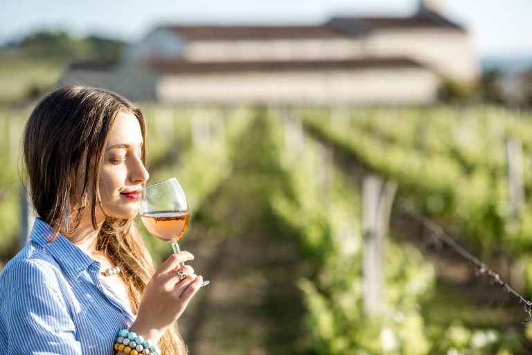 Femeie degust&acirc;nd un pahar de vin ros&eacute; &icirc;ntr-o podgorie, bucur&acirc;ndu-se de aromele vinului rom&acirc;nesc.